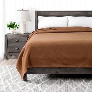 May include: A brown wool blanket on a bed with a wooden headboard and white pillows. The blanket has a subtle texture and a dark brown border.