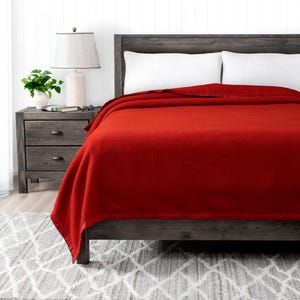 May include: A red wool blanket on a bed with a wooden headboard. The blanket is folded back to show the red color and texture.