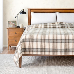 Peut inclure: Une couverture en plaid brun et blanc sur un cadre de lit en bois avec des oreillers blancs. Le lit est dans une chambre avec une table de chevet en bois et une lampe.