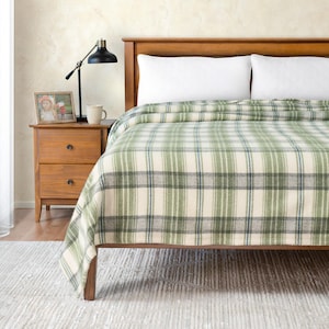 May include: A green and white plaid throw blanket on a wooden bed frame. The blanket is folded at the foot of the bed and has a subtle blue and gray pattern.