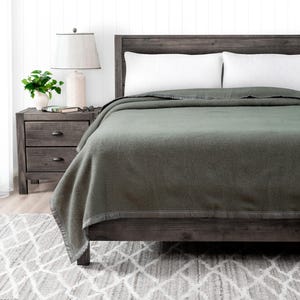 May include: A dark green wool blanket on a wooden bed frame with white pillows. The blanket has a dark gray border.