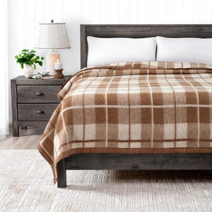 May include: A brown and white plaid throw blanket on a bed with white pillows. The blanket has a brown border.