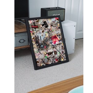 May include: A framed collage of colorful images and text, including the words "Liberte" and "Sicilia". The collage is set against a white background and is framed in black.
