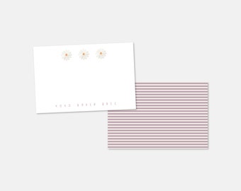 May include: A white card with three small white daisies printed on it. The card has the text "XOXO DAVEY OPIE" printed in black at the bottom. The card is sitting on top of a purple and white striped background.