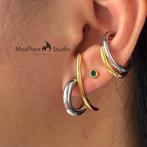 May include: Earrings in silver and gold tones. One earring is a curved design, the other is a double hoop. A small green stud earring is also visible. The MoxFlare Studio logo is in the image.