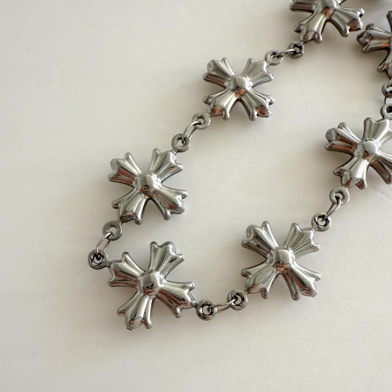 May include: A silver chain necklace with multiple silver cross charms. The cross charms have a detailed design with pointed edges.