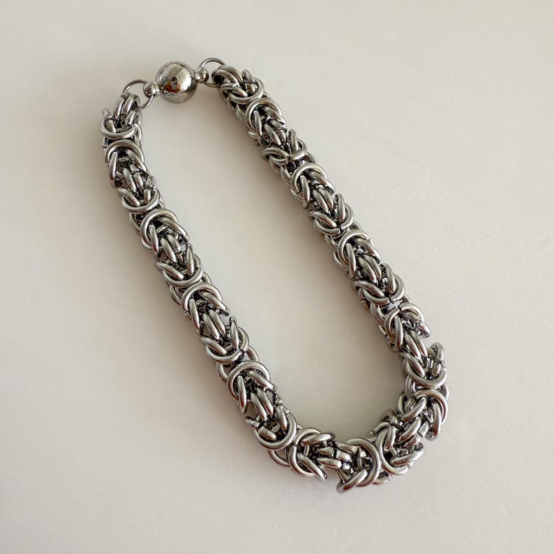 Pu&ograve; includere: Un braccialetto a catena argentato con chiusura magnetica. La catena &egrave; realizzata con anelli di metallo intrecciati.