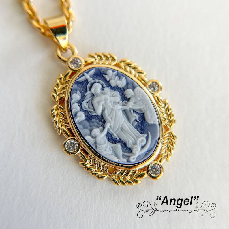 May include: Gold pendant necklace with a blue and white cameo featuring a religious figure with angels. The pendant is surrounded by a gold leaf design and has clear rhinestones.
