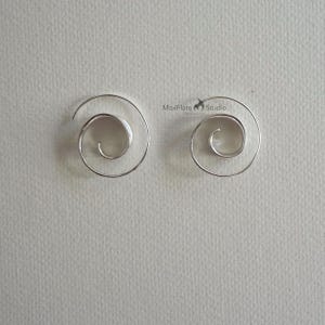 May include: A pair of silver spiral earrings. The earrings are in a spiral shape, with a smooth, polished finish. The earrings are displayed on a light grey background. The earrings are from MoxFlare Studio.