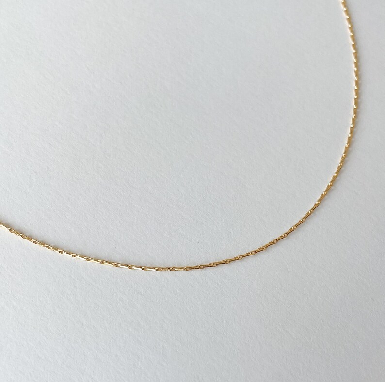 May include: A delicate gold chain necklace with a simple, box chain design.