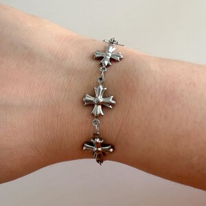 May include: A silver bracelet with a chain link design and multiple cross-shaped charms.