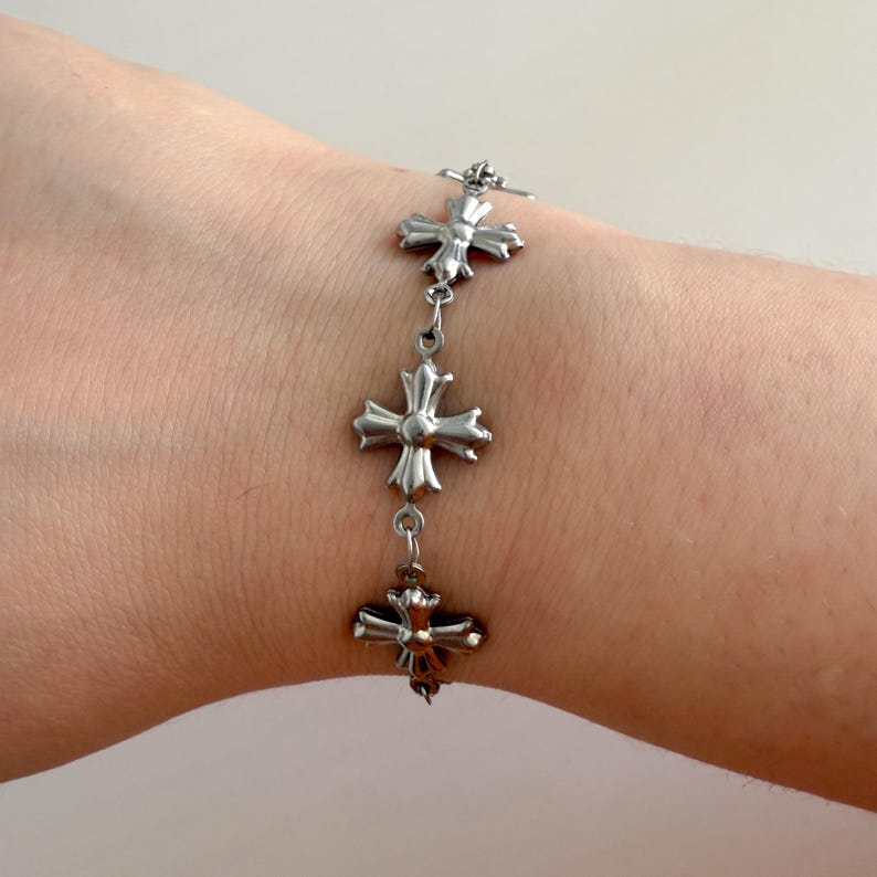 May include: A silver bracelet with a chain link design and multiple cross-shaped charms.
