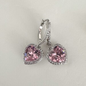 May include: A pair of silver dangle earrings with pink heart-shaped stones surrounded by a halo of smaller clear stones.