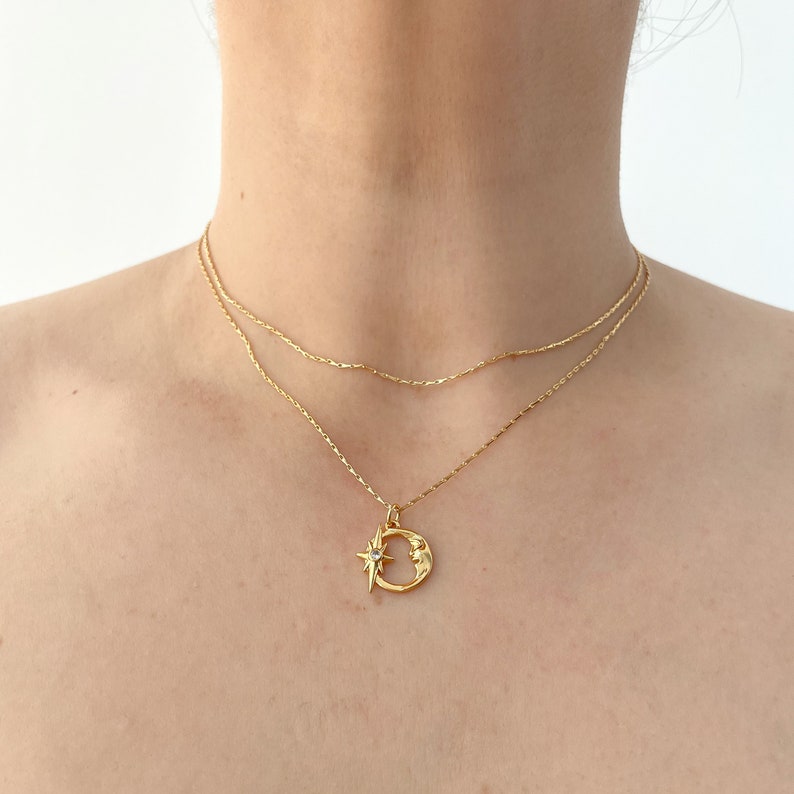 May include: A gold chain necklace with a crescent moon pendant featuring a small star with a clear stone in the center.