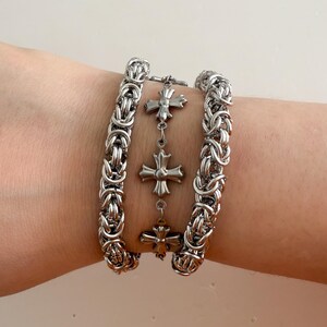 Pu&ograve; includere: Tre braccialetti a catena d'argento con un braccialetto con ciondoli d'argento con quattro ciondoli a forma di croce.