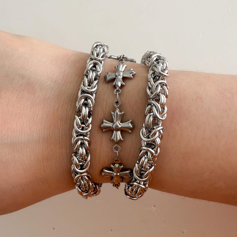 Pu&ograve; includere: Tre braccialetti a catena d'argento con un braccialetto con ciondoli d'argento con quattro ciondoli a forma di croce.