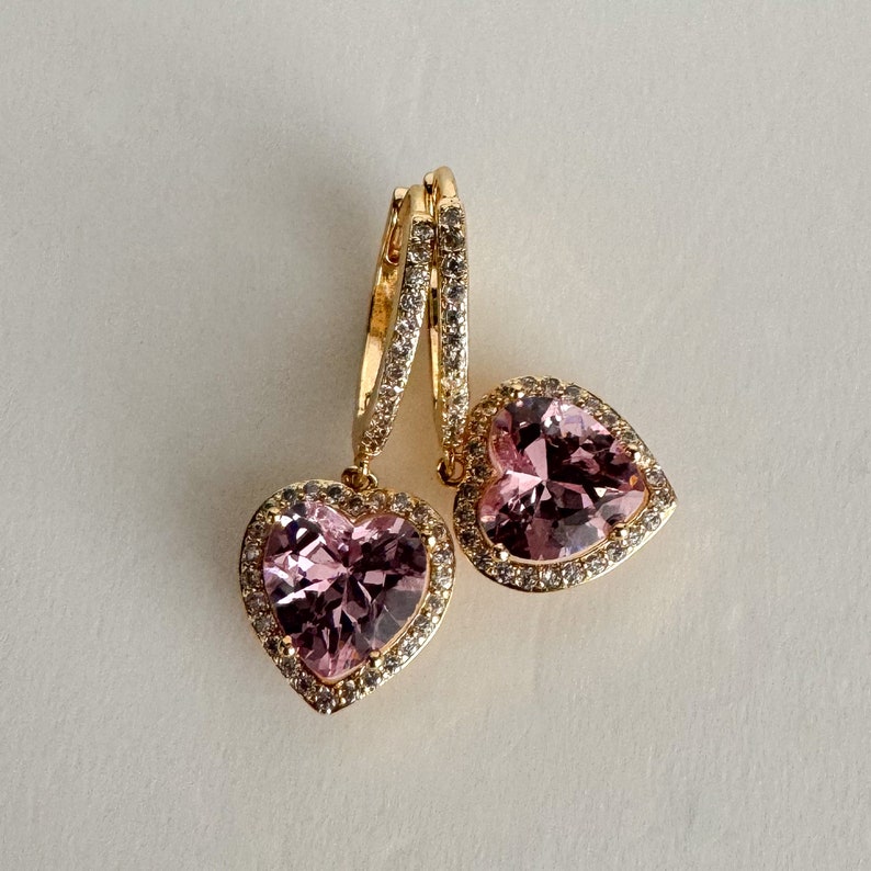 May include: A pair of gold heart-shaped earrings with pink gemstones and clear crystal accents.