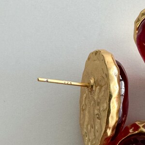 May include: A pair of red glass earrings with gold-toned metal settings. The earrings have a textured, hammered look and are marked "925" on the back.