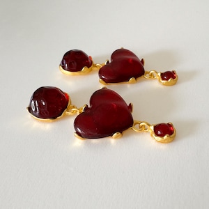 May include: A pair of dangle earrings with red glass heart-shaped charms and smaller red glass round charms. The earrings are gold-toned.