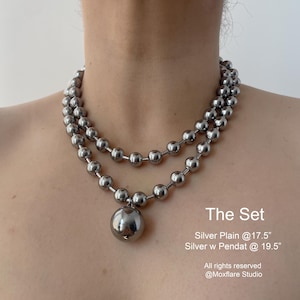 May include: Two silver chain necklaces with a large silver pendant. The top chain is 17.5 inches long and the bottom chain is 19.5 inches long. The set is called "The Set".
