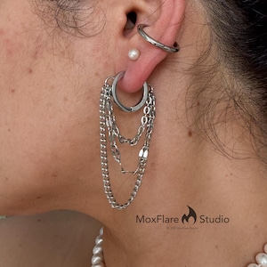 May include: Silver hoop earrings with dangling chains. The earrings are attached to a pierced ear, with a small pearl stud and a silver ear cuff visible. The MoxFlare Studio logo is in the bottom right corner.