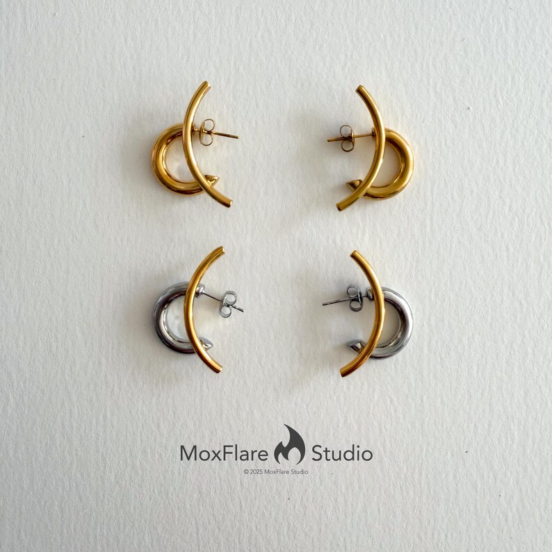 May include: Four pairs of earrings. Two pairs are gold-toned, featuring a curved bar and a circular element. The other two pairs are silver-toned, with a gold-toned curved bar and a silver circular element. The MoxFlare Studio logo is at the bottom.