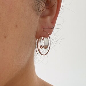 May include: Silver spiral earrings with a wrapped design. The earrings have a unique, open design with a coiled centre. The earrings are shown on a person's ear, with the MoxFlare Studio logo visible in the background.