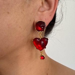 May include: Red glass heart shaped earrings with a smaller red glass bead dangling from the bottom. The earrings are gold toned.