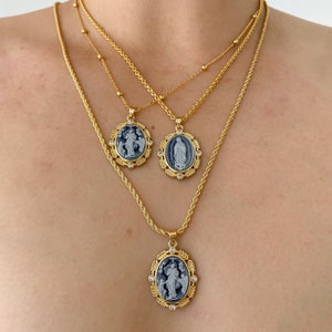 May include: Three gold chain necklaces with oval pendants featuring religious imagery. The pendants are adorned with clear rhinestones and have a blue enamel background.