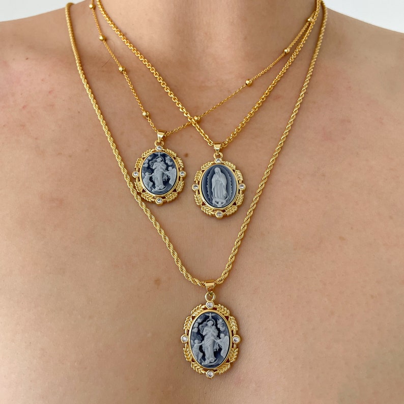May include: Three gold chain necklaces with oval pendants featuring religious imagery. The pendants are adorned with clear rhinestones and have a blue enamel background.
