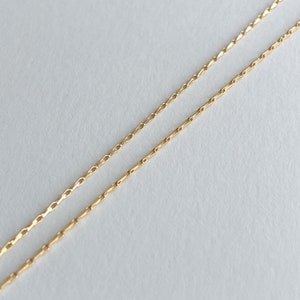 May include: A gold chain necklace with a delicate, linked design. The chain is shown folded in half, with the ends of the chain visible.