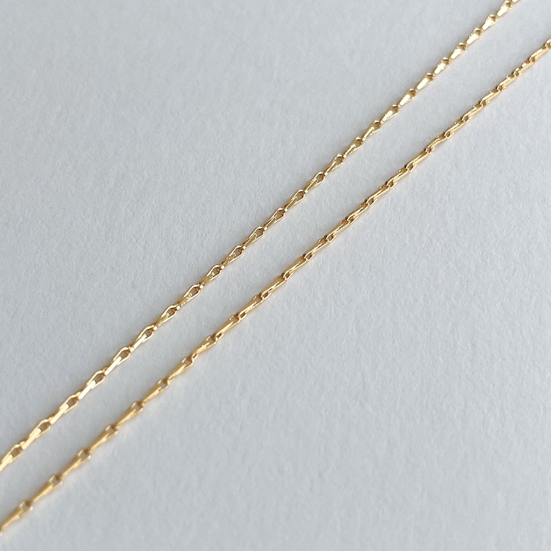 May include: A gold chain necklace with a delicate, linked design. The chain is shown folded in half, with the ends of the chain visible.