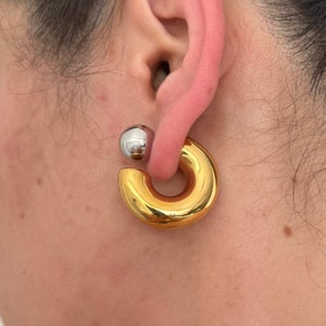 May include: A gold hoop earring with a silver ball on the top. The earring is worn in the earlobe.