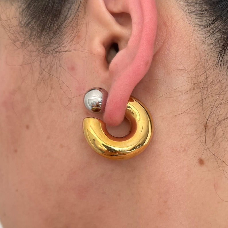 May include: A gold hoop earring with a silver ball on the top. The earring is worn in the earlobe.
