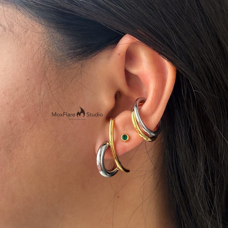 May include: Earrings in silver and gold tones. One earring is a curved design, the other is a double hoop. A small green stud earring is also visible. The MoxFlare Studio logo is in the image.