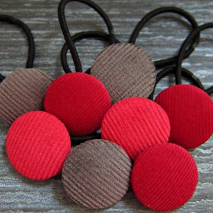 Könnte beinhalten: Acht Haargummis mit stoffbezogenen Knöpfen. Vier Knöpfe sind rot und vier sind braun.