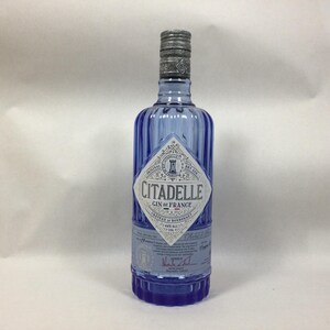 May include: A blue Citadelle Gin bottle with a silver cap. The bottle has a diamond-shaped label with the brand name and "Gin de France" printed on it. The bottle is approximately 10 inches tall.