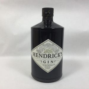 May include: A dark brown glass bottle of Hendrick's Gin with a diamond-shaped cream label. The label features black text, a botanical illustration, and states 750 ml, 44% alc. by vol., and est. 1886. The bottle has a black cap.