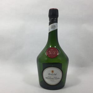 May include: A green glass bottle with a black cap and a red wax seal. The bottle has a label that reads "D.O.M. BÉNÉDICTINE". The bottle is empty and has a unique shape.