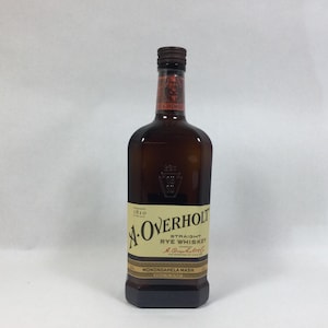May include: A brown glass bottle of A. Overholt Straight Rye Whiskey. The label is cream-colored with black text and a gold border. The bottle has a dark brown cap and a rectangular base. The label reads "MONONGAHELA MASH."