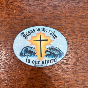 May include: A blue and white round sticker with a yellow sunburst behind a black cross. The sticker says "Jesus is the calm in our storm" with the scripture reference "Matthew 14:24-33" underneath.