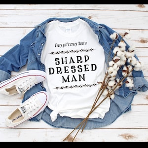 May include: White t-shirt with the text "Every girl's crazy 'bout a SHARP DRESSED MAN" in black lettering with a geometric design above and below the text.