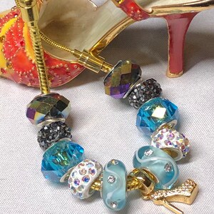 May include: A gold charm bracelet with a variety of colourful beads, including blue, white, and iridescent. The charm is a gold high heel shoe.