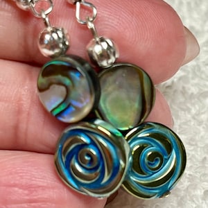 May include: A pair of silver dangle earrings with abalone shell and blue swirl beads. The earrings have a silver hook fastening.