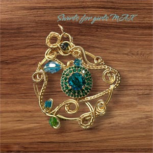 Peut inclure: Un pendentif en fil d'or avec une grande pierre précieuse bleue entourée de petites pierres précieuses vertes. Le pendentif a la forme d'un tourbillon et présente un design délicat.