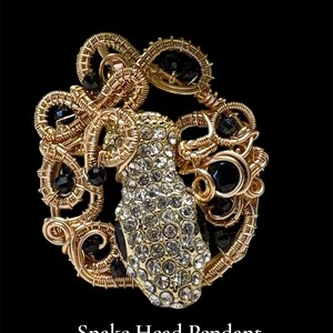 Peut inclure: Pendentif en fil d'or avec une tête de serpent. La tête de serpent est incrustée de cristaux transparents et le pendentif est orné de perles noires. Le texte "Snake Head Pendant" est en bas.