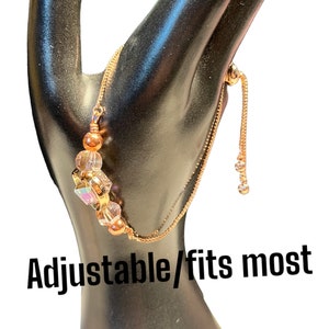 May include: An adjustable rose gold bracelet with a crystal charm and beads. The bracelet is on a black mannequin hand. "Adjustable/fits most" is written below the bracelet.