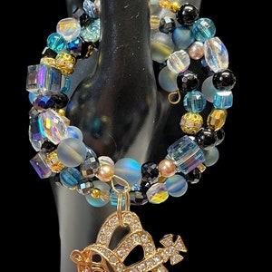 May include: A multi-strand bracelet featuring blue, black and gold beads. The bracelet has a charm in the shape of a crown with the word "Queen" on it.