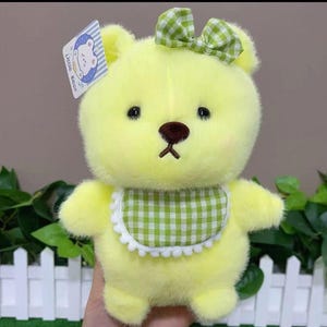 Puede incluir: Un oso de peluche amarillo con un lazo y babero de cuadros verdes. El oso tiene una nariz marr&oacute;n y ojos negros. Una etiqueta que dice "Little Bear" est&aacute; adjunta al oso.