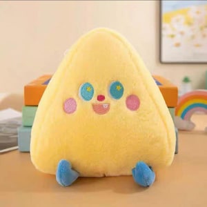 Puede incluir: Un cojín de felpa amarillo en forma de triángulo con rasgos faciales bordados. Tiene ojos azules con detalles de estrellas amarillas, mejillas rosas y una boca sonriente. Se ven pequeños pies azules en la parte inferior. El cojín está diseñado para parecerse a un personaje amigable.